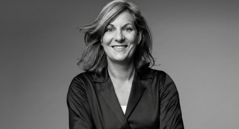 Porträt einer lächelnden Frau mit blonden Haaren in einem weißen Hemd, Hände in der Taille.